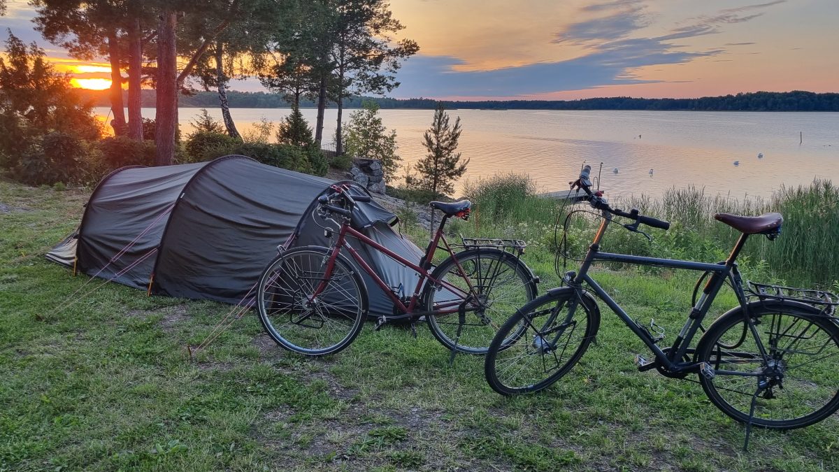 Zwei Fahrräder uns ein Zelt stehen im Sonnenuntergang am Wasser