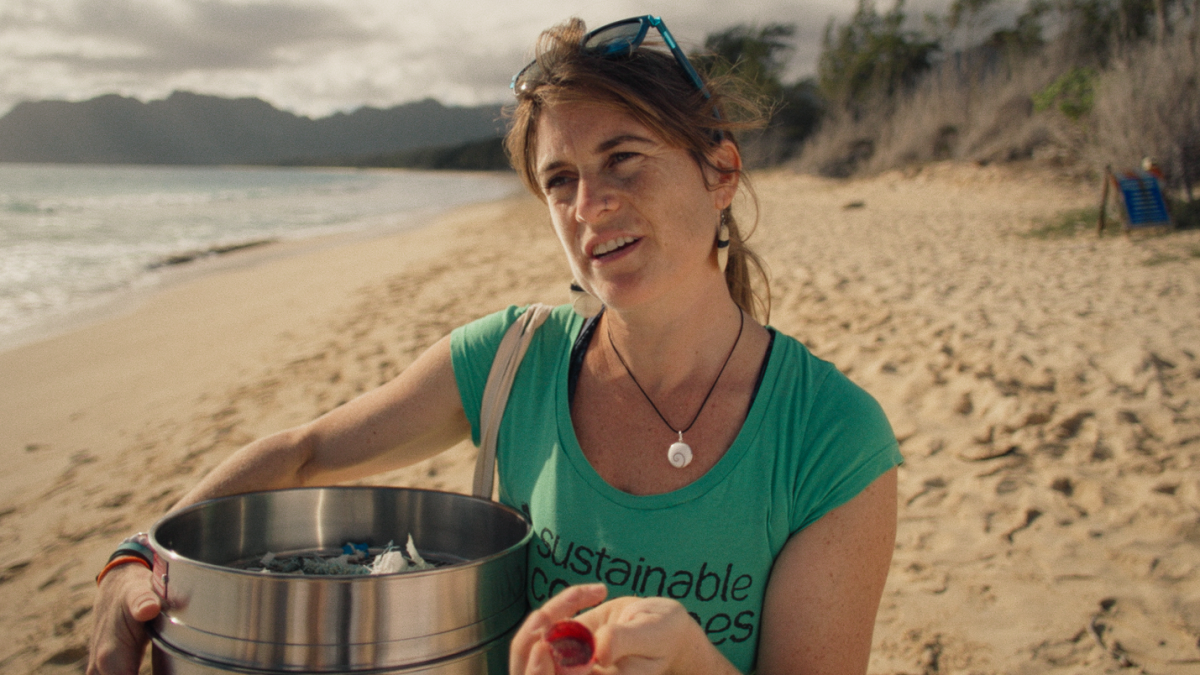 Eine Frau steht am Strand und hat einen Eimer mit Plastikmüll in der Hand