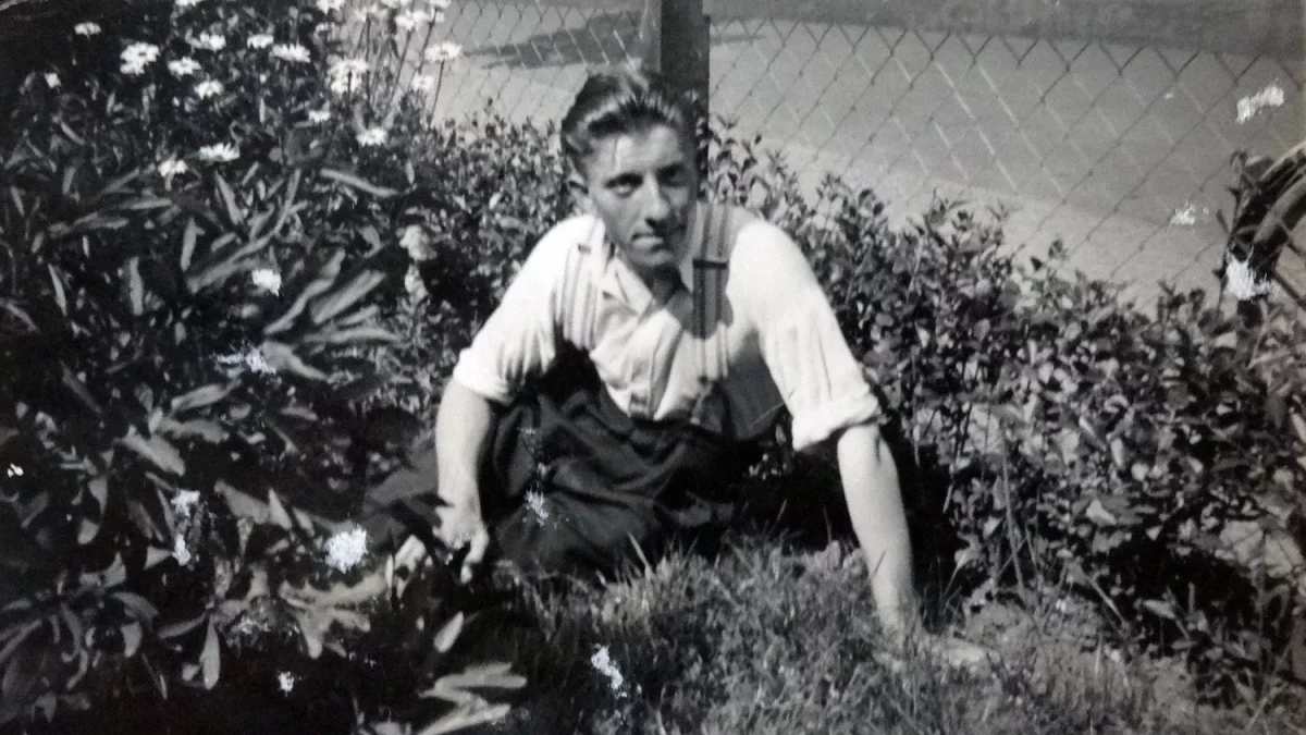 Altes schwarz-weiß Bild von einem Jungen Mann, der zwischen Büschen in einem Garten sitzt.