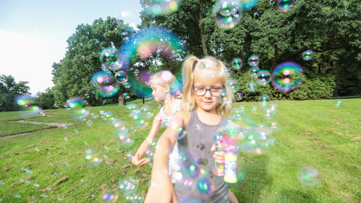 Zwei Kinder spielen im Grünen mit Seifenblasen